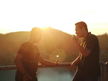 Smiling friends talking against sky during sunset