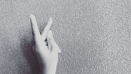 Cropped hand of person showing peace sign against wall