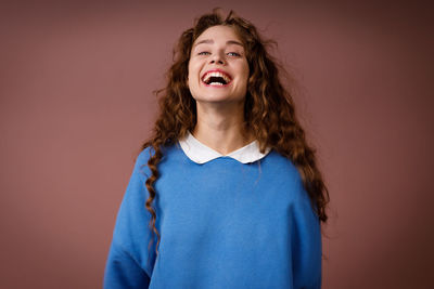 Portrait of young woman standing against pink background