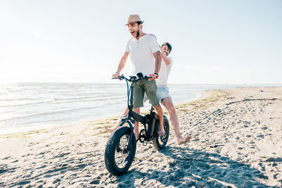 Rear view of woman riding bicycle on beach against sky