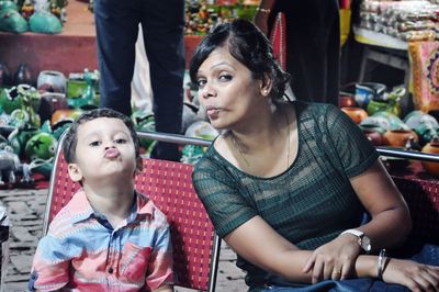 Portrait of mother and son puckering lips while sitting on chair against market
