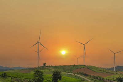 Wind turbines on field against sky during sunset