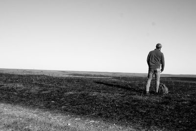 Rear view of man standing on field against clear sky