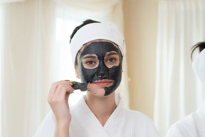 Young woman removing facial mask from face in spa