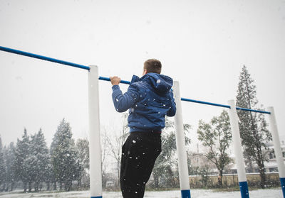 Rear view of man exercising at park during snow fall