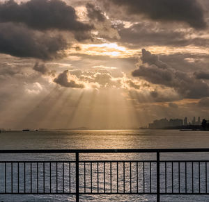 Sunlight streaming through railing against sea during sunset