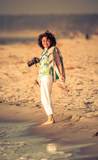 Portrait of smiling woman with digital camera standing at beach