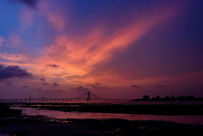 Silhouette bridge over land against sky during sunset