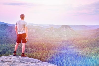 Hiker or running man hold plastic bottle with drink on rocky edge at misty mountains background