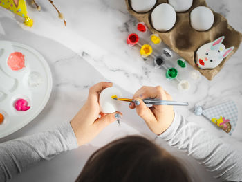 Hands of a girl in a gray turtleneck, paint an easter egg with a brush and acrylic paint 