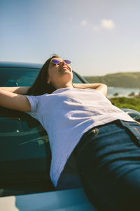 Young woman lying on car at beach