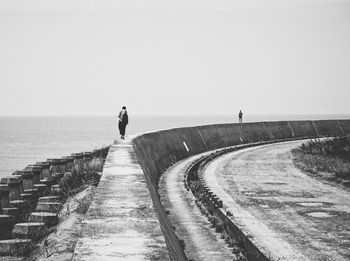 Person walking on retaining wall by sea against clear sky