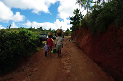 Rear view of boys walking on road against sky