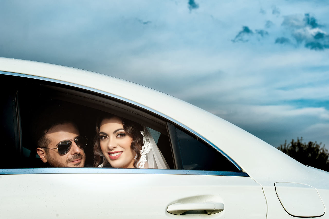 PORTRAIT OF A SMILING YOUNG COUPLE ON CAR