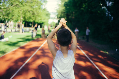 Rear view of boy with arms raised and hands clasped standing at park