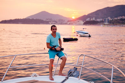 Portrait of man sitting on boat railing in sea during sunset