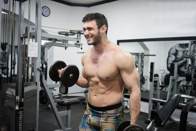 Shirtless man lifting dumbbells in gym