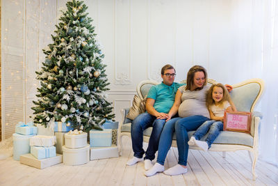 Happy family sitting on sofa by christmas tree