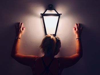 Rear view of woman standing by illuminated lighting equipment on wall