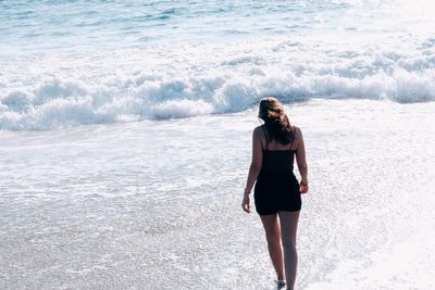 Rear view of young woman walking at beach on sunny day