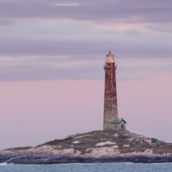 Lighthouse by sea against sky during sunset