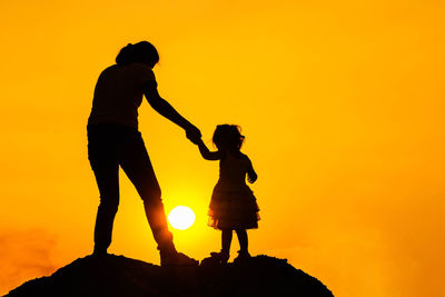 Silhouette people standing on rock against orange sky