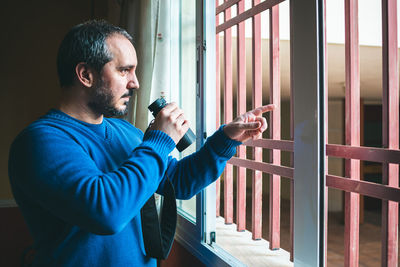 Man with binoculars standing by window at home