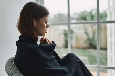 Side view of woman looking away against window