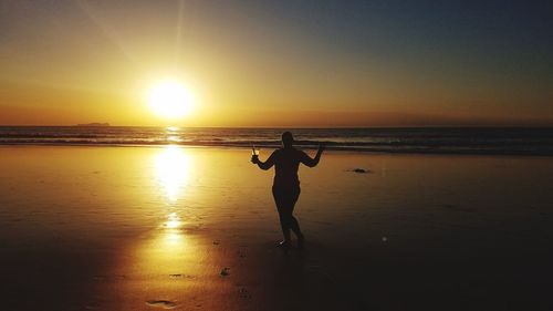 Silhouette woman standing at beach against sky during sunset