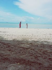 Woman playing with son at sandy beach against cloudy sky