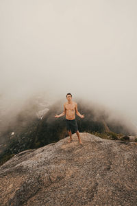 Shirtless young man standing on mountain against sky