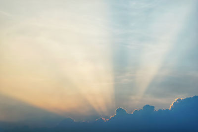 Low angle view of sunlight streaming through clouds during sunset