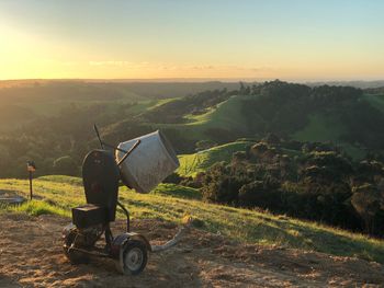 Machinery on hill against sky during sunset