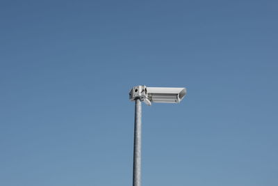 Low angle view of surveillance camera against clear blue sky