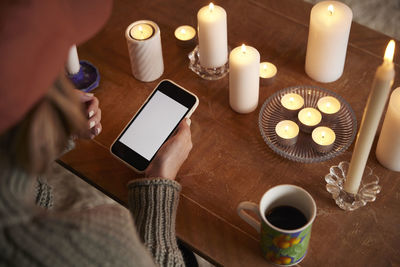 Woman using phone next to lit candles