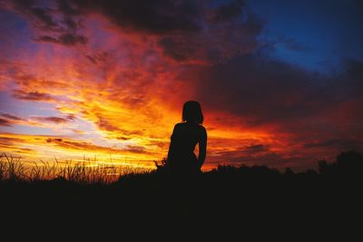 Silhouette man standing on field against orange sky