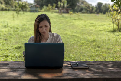 Young woman using laptop while sitting on field