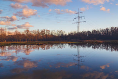 Reflection of electricity pylon in lake against sky