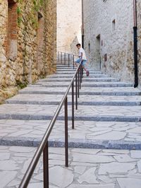 Boy sitting on railing amidst buildings 