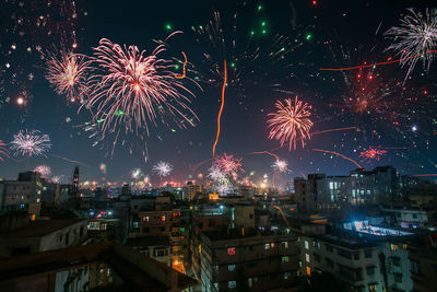 Firework display in city against sky at night