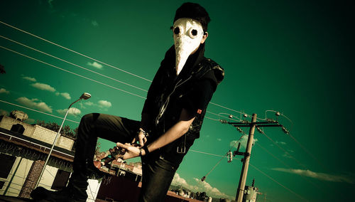 Man wearing mask while holding musical instrument against sky