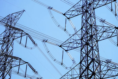 Low angle view of electricity pylons against clear blue sky