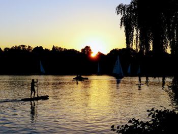 Silhouette man standing by lake against clear sky during sunset