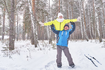 Happy mature couple in sportswear having fun in snowy forest. man lifted woman onto his shoulder