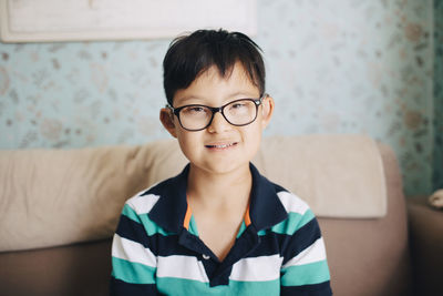 Portrait of disabled boy sitting on sofa against wall at home