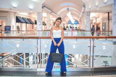 Portrait of teenage girl standing against railing in mall