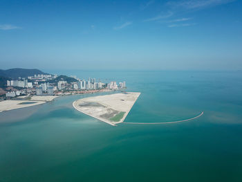 Aerial view of city by sea against blue sky