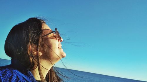 Portrait of young woman looking away against blue sky