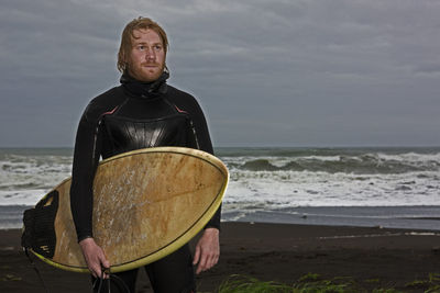 Young man walks with surfboard along beach in iceland