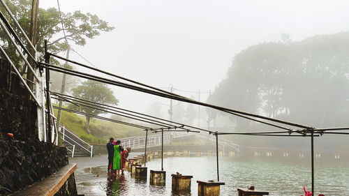 Rear view of people on bridge against sky during rainy season